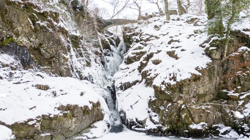A view of the frozen waterfall at Aira Force in winter, surrounded by snow
